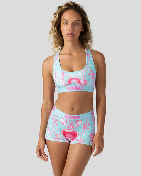 Woman wearing light blue and pink patterned sports bra and shorts set with PSD branding.