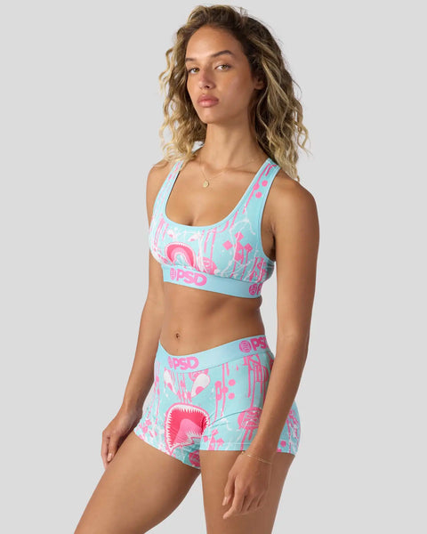 Woman wearing turquoise and pink patterned sports bra and matching skirt with geometric print design.