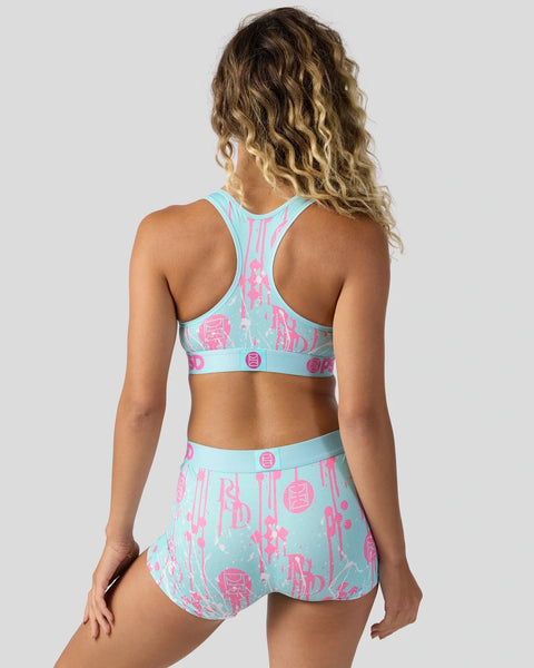 Woman wearing light blue sports bra and shorts with pink geometric print design, shown from behind.