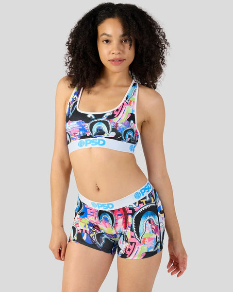 Woman wearing colorful graphic sports bra and shorts set with white waistband trim.