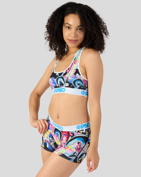 Woman wearing a colorful shark-patterned sports bra and matching shorts with blue and white trim.