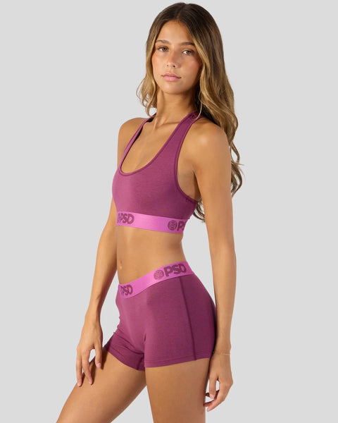 Woman wearing a magenta purple racerback sports bra and matching shorts with branded waistband.