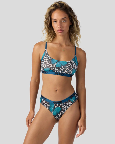 Woman wearing a two-piece swimsuit with blue straps and a leopard print pattern with turquoise butterfly graphics.