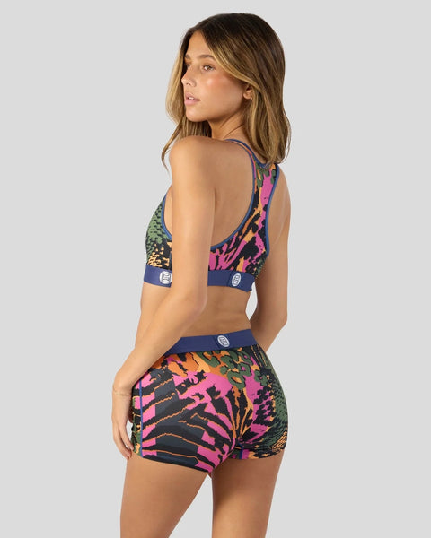 Woman wearing a colorful patterned sports bra and matching shorts set with pink, navy, yellow, and green abstract designs.
