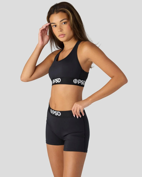 Woman wearing black sports bra and shorts with white branding on elastic bands.