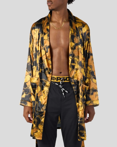Man wearing gold and black silk robe with abstract pattern over black pants and chain necklace.