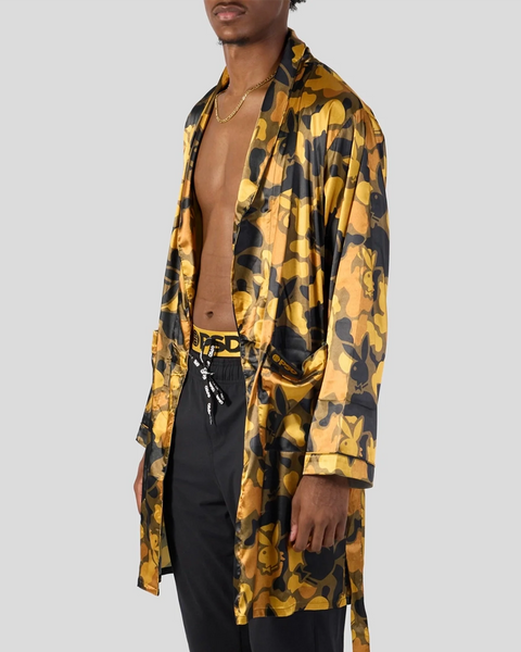 Man wearing gold and black Playboy patterned silk shirt over black pants with chain necklace.