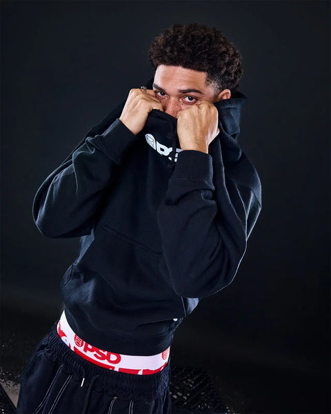 Black Playboy hoodie with red and white waistband tag worn by male model against dark background.