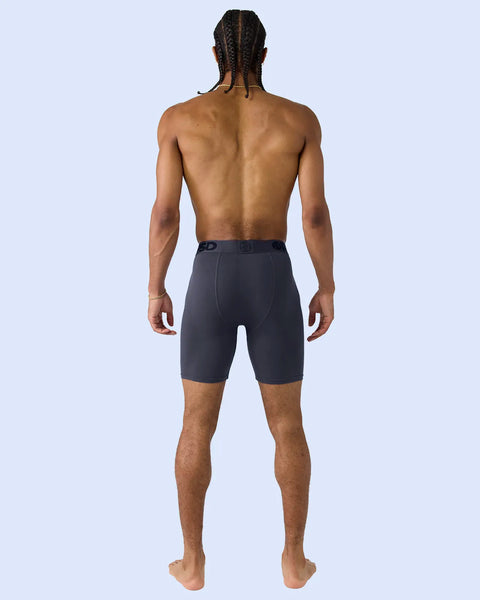 Man wearing dark purple shorts shown from back view against light blue background.