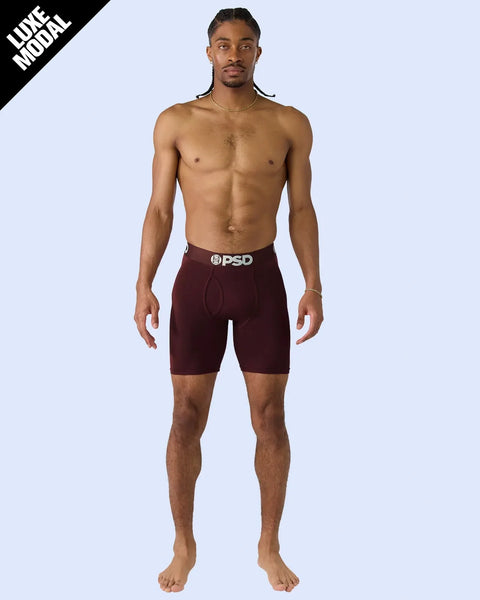 Man wearing burgundy modal shorts with PSD waistband on light blue background.