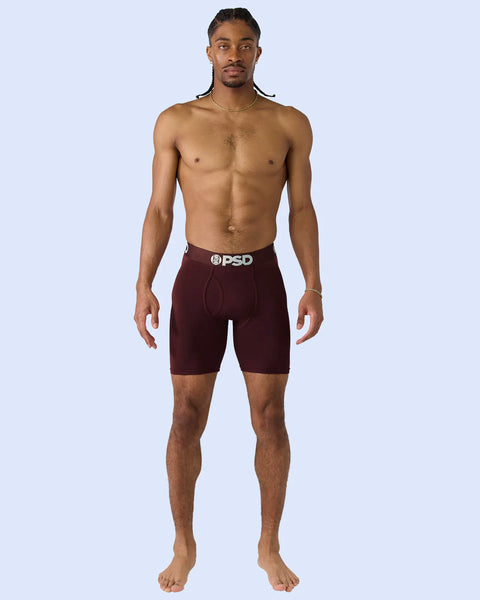 Man wearing dark burgundy boxer briefs with PSD waistband against light blue background.