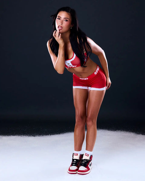 Woman wearing red and white sports bra and shorts set with matching sneakers against dark background.