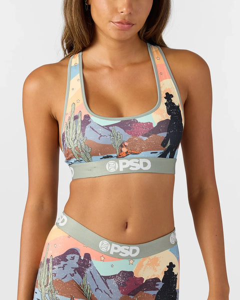 Women's sports bra with desert landscape print featuring cacti, mountains, and stars in peach, blue, and purple tones.