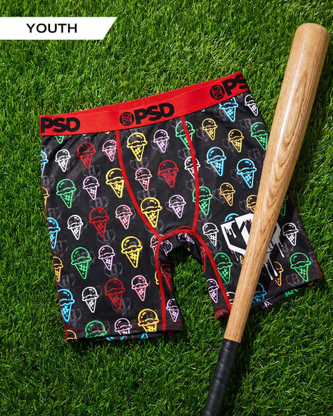 Youth boxer shorts with colorful ice cream cone print and red waistband, displayed with wooden baseball bat on grass.
