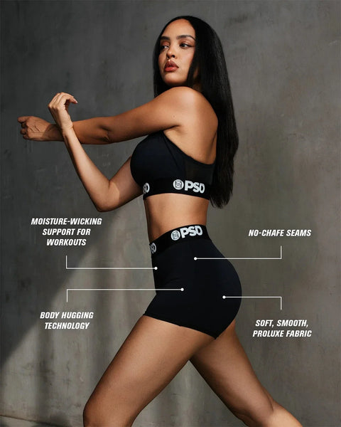 Woman wearing black ProLuxe sports bra and shorts with branded waistband against gray background.