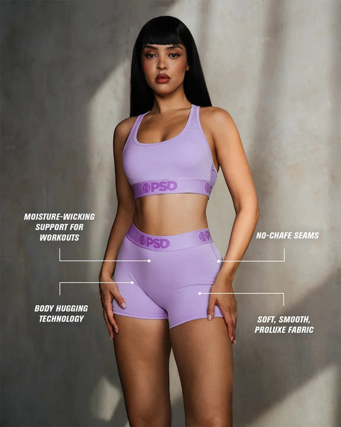 Woman wearing lavender racerback sports bra and matching shorts with branded waistband.