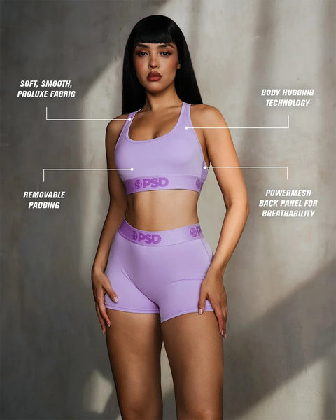 Woman wearing lavender sports bra and shorts set with removable padding and mesh back panel.