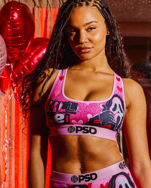 Woman wearing pink sports bra and matching underwear with ghost face graphic design against red neon lighting.